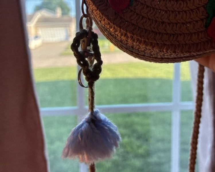 Fluffy periwinkle-blue yarn pom-pom charm hanging from a straw bag