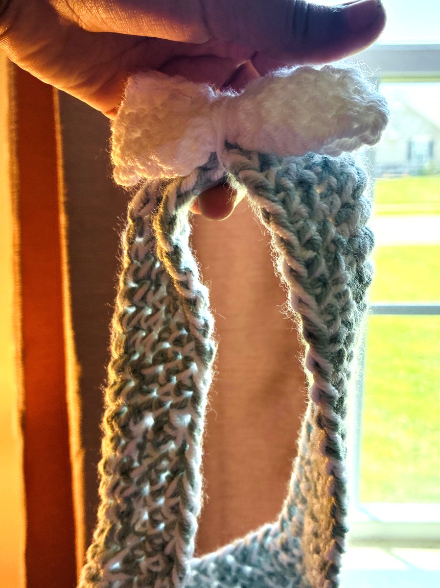 Sage crochet bow headband held up in golden window light