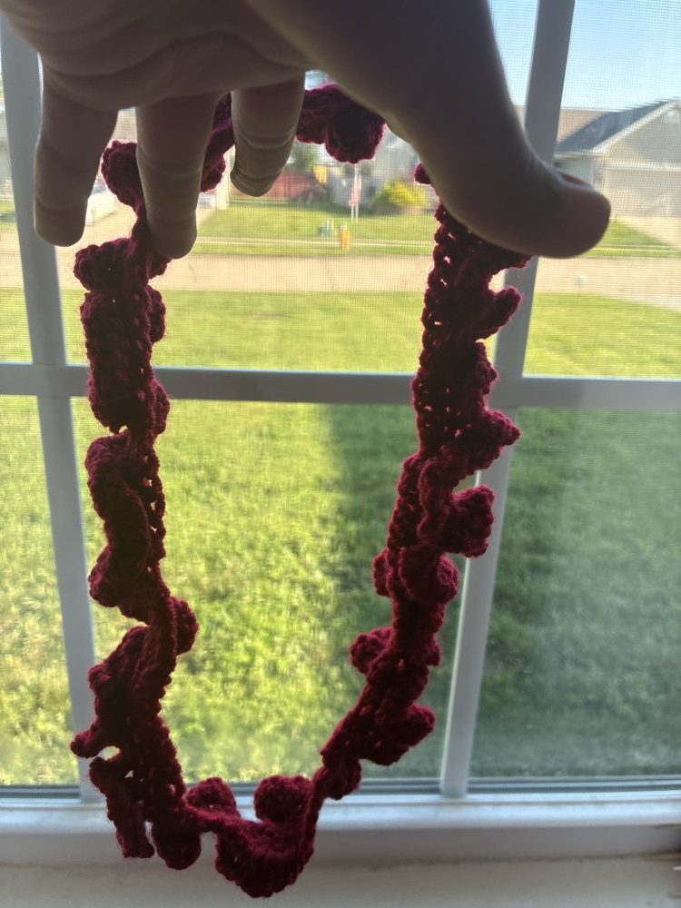 Deep burgundy crochet ruffle headband held up to the light