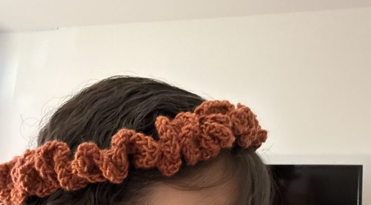 Rust-orange crochet ruffle headband worn like a little flower crown