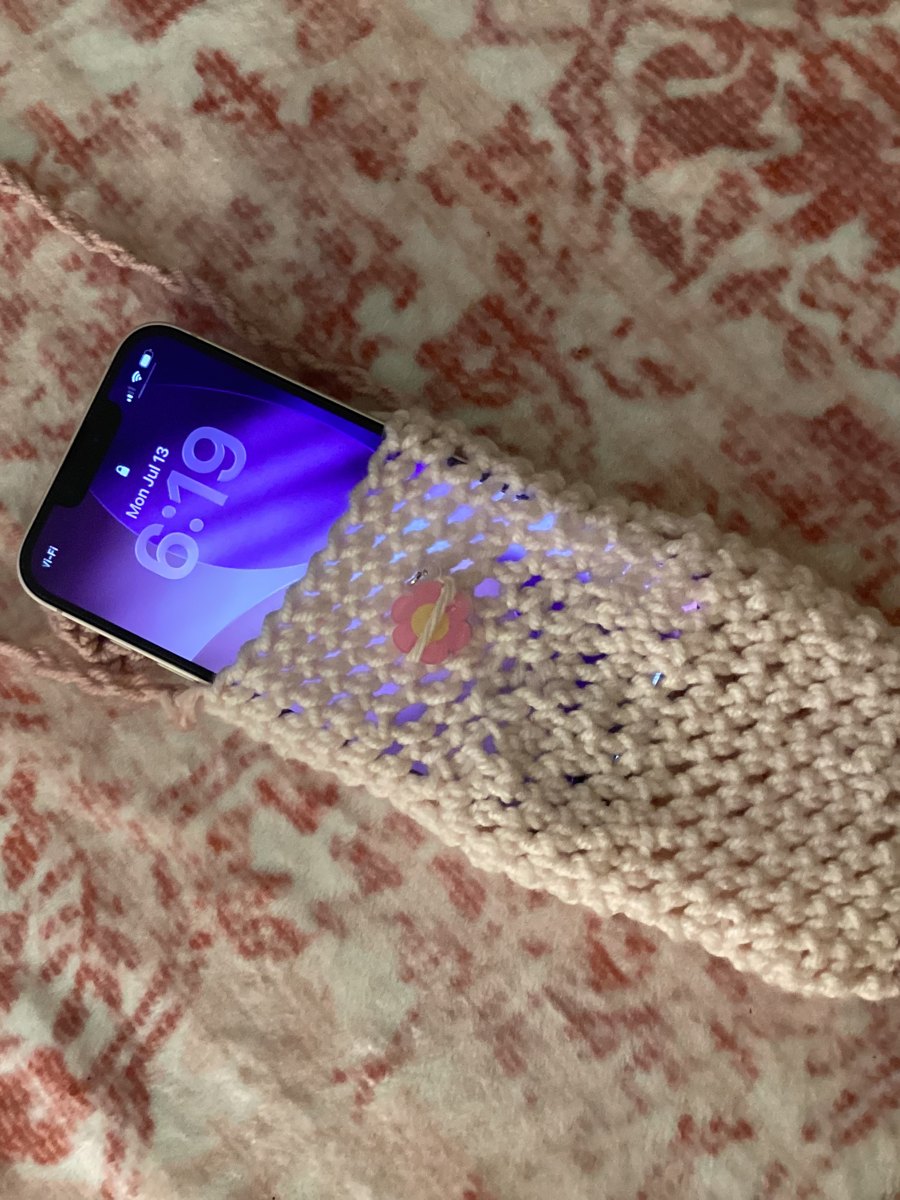 Phone tucked into a cream crochet phone bag with a little pink flower button